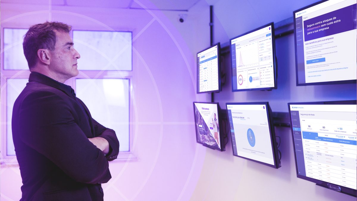 CEO da PSafe em pé olha para uma série de telas na parede que exibem gráficos e métricas
