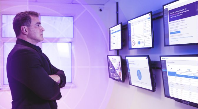 CEO da PSafe em pé olha para uma série de telas na parede que exibem gráficos e métricas