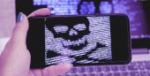 Tela de um smartphone com o desenho de uma caveira formada por códigos diante da tela de um laptop